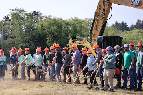 A line of people wearing hardhats pose with shoves in front of construction equipment