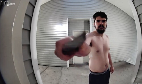 A shirtless man with a bushy beard holds a knife up to a doorbell camera.