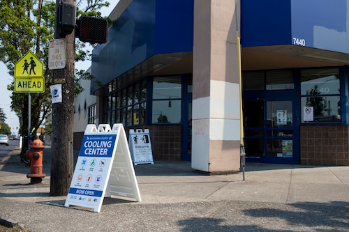 The exterior of a building with blue awnings.  In front of it, a sign says "Cooling center"